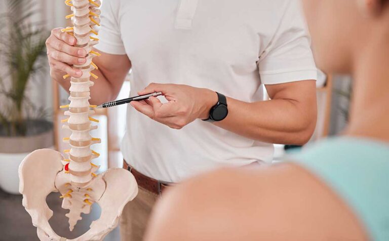 Adult receiving gentle back mobility treatment beside a spine model in a clinical room.