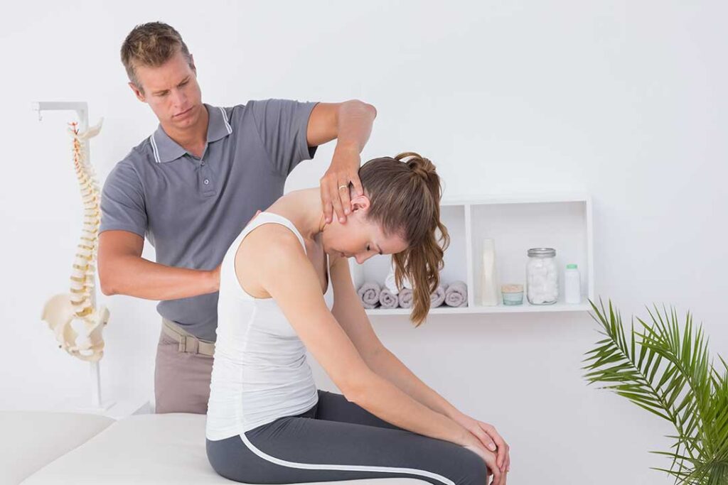 Person gently turning their neck beside a desk, with one hand resting on the upper shoulder.